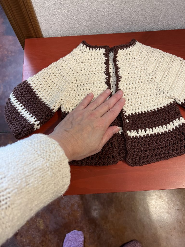 A crocheted baby sweater with my hand (6 inches from base to tip) for scale.