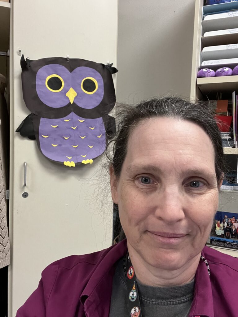 purple paper owl in background with smiling person, long hair pulled back.