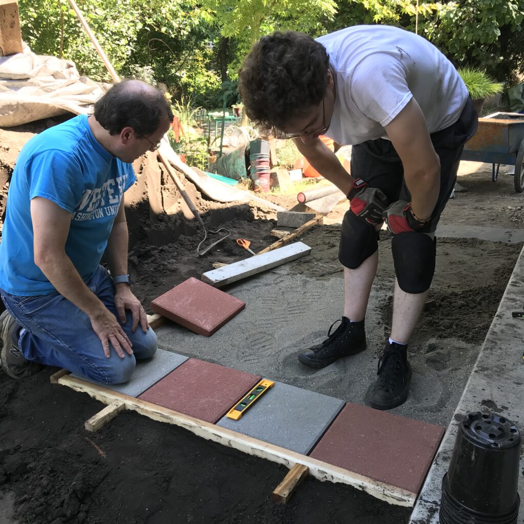 Grant and Tom placing pavers for the patio extension in front of the main entry, The pavers are 12 inch squares and alternate red and gray.